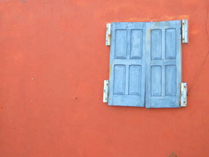 Orange wall with a window with blue shutters