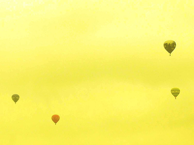 Four hot air balloons against a yellow sky