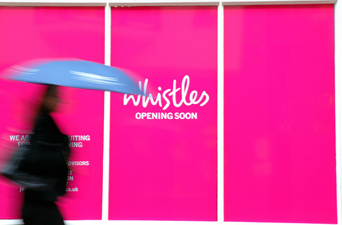 Woman with umbrella walking in front of a pink store window