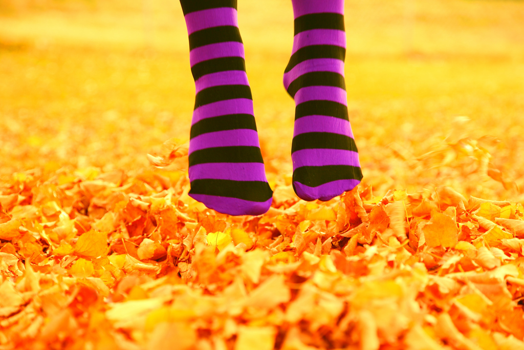 Feet with striped socks jumping over autumn leaves